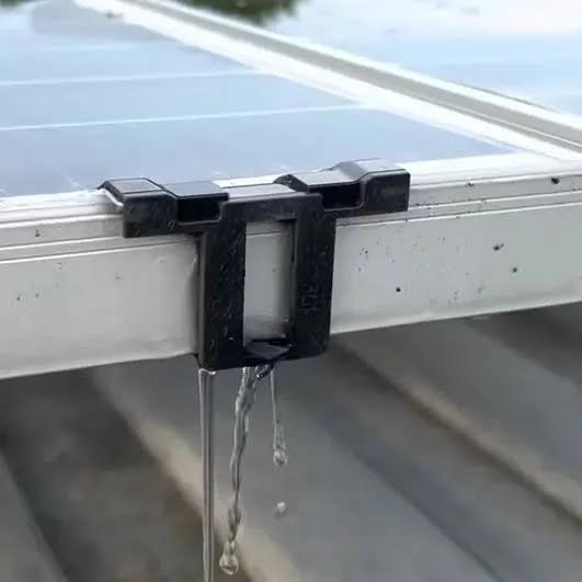 Black solar clip attached to a solar panel with water droplets falling from the clip’s edge.