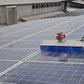 Silver steel solar panel cleaning robot spraying water while scrubbing with a blue rotating brush