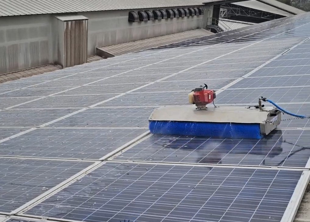 Silver steel solar panel cleaning robot spraying water while scrubbing with a blue rotating brush