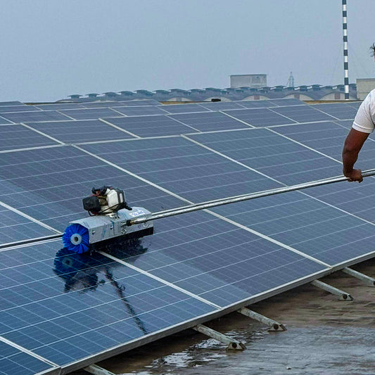 Man operating a silver steel solar cleaning robot with a blue rotating brush to clean a rooftop solar panel