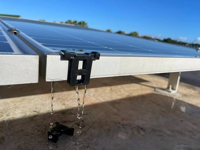 Dark gray solar clip attached to a solar panel with water droplets falling from it.