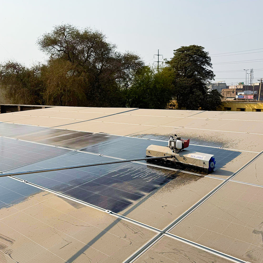 Silver steel solar cleaning robot with blue rotating brush removing heavy dust and dirt from a solar panel surface