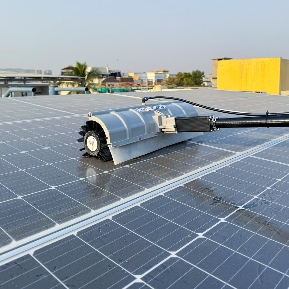 An electric rotating solar cleaning brush with a silver brush head and black handle being used on a solar panel.