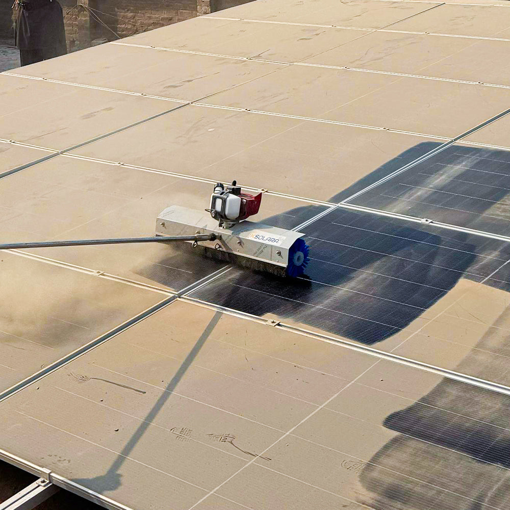 Silver steel solar cleaning robot with blue rotating brush removing heavy dust and dirt from a solar panel surface