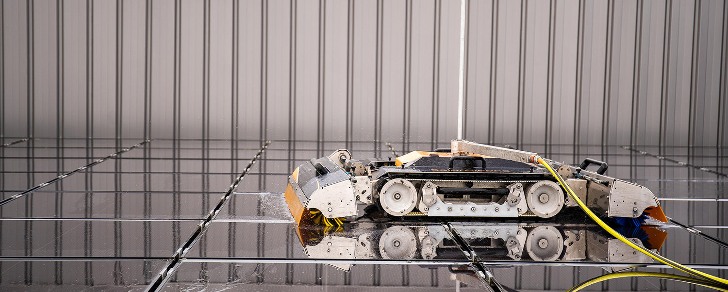 Side profile of SolarCleano F1 cleaning a solar panel, highlighting its compact body, tracks, and brush roller in contact with panel surface.
