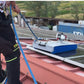 Man cleaning solar panels on a red roof using a silver metal solar cleaning robot with blue rotating brushes