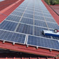 Silver steel solar cleaning robot with blue rotating brush cleaning solar panels on a red-colored rooftop
