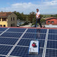 Man using a silver steel solar cleaning robot with blue rotating brush to clean solar panels on a rooftop.