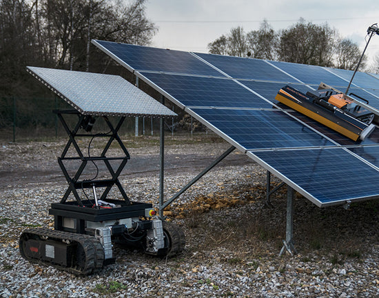 One solar cleaning robot actively operating on a solar panel, while another robot with rotating wheels rests idle on the ground nearby